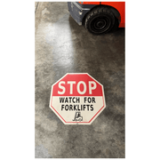 Watch for forklifts floor sign on warehouse floor with forklift traffic in background