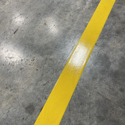 4" yellow mighty line tac tape adhered to  industrial floor with glare to show diamond plate texture of the traction tape.